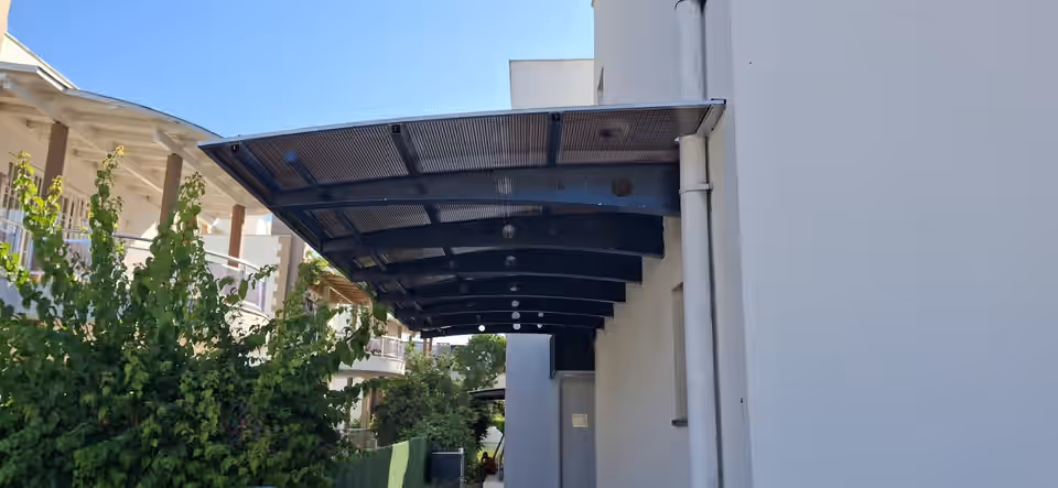 Cephe boyunca uzanan metal taşıyıcılı yarı saydam sundurma