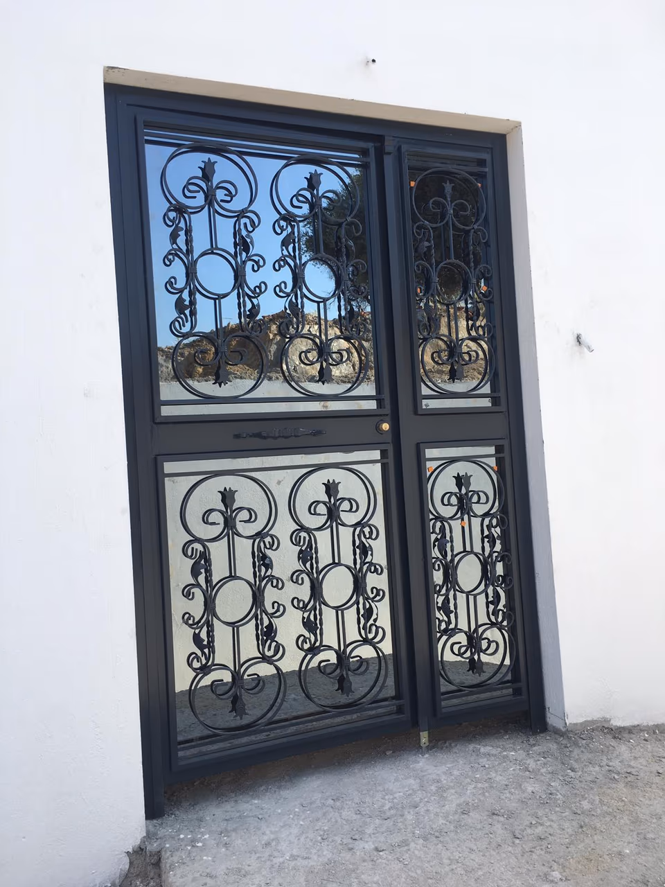 Kıvrımlı ferforje desenleri bulunan siyah camlı giriş kapısı