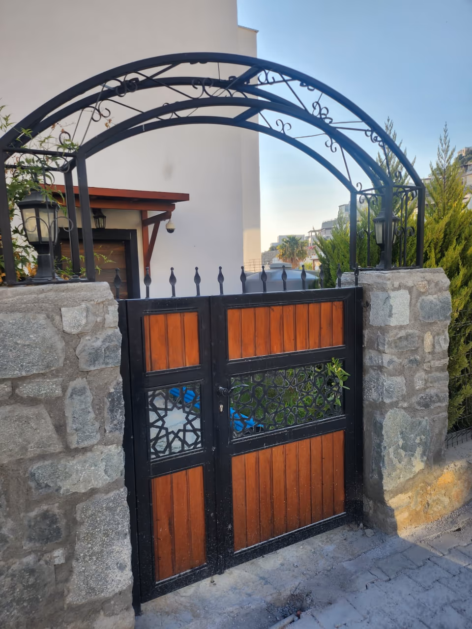Taş duvar arasında üstü kemerli, ahşap panelli metal bahçe kapısı